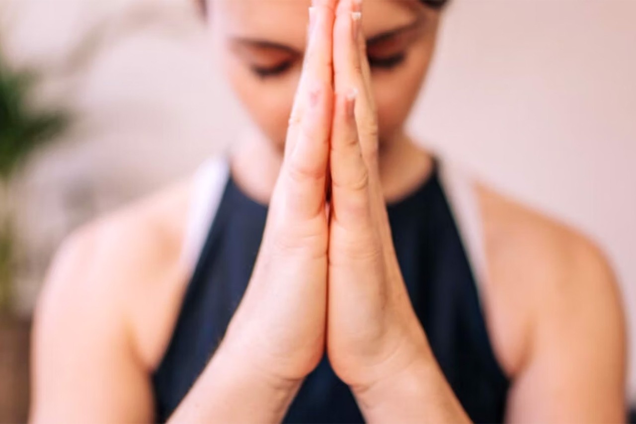 Woman in a meditation pose with hands together in front of face, eyes closed