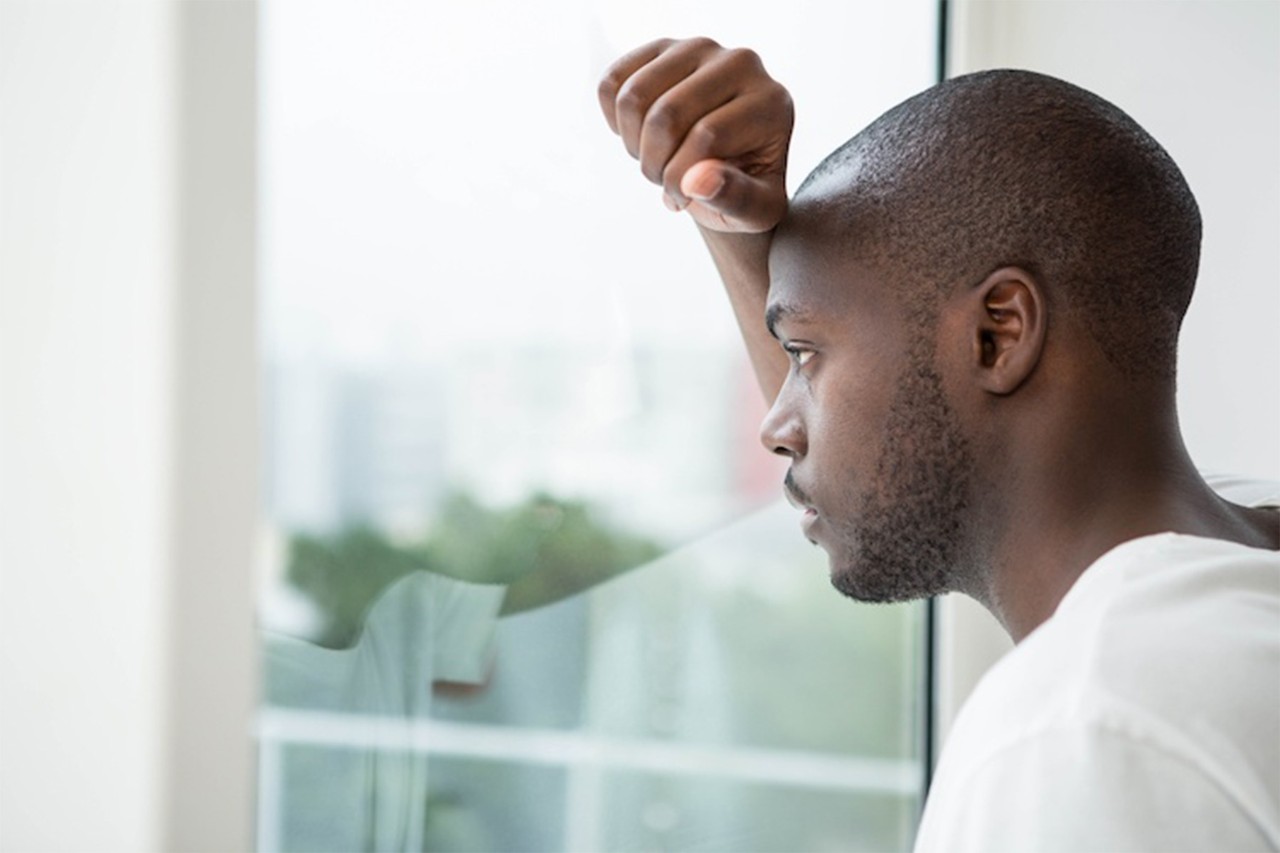Man leaning on a window, looking outside with a thoughtful or concerned expression