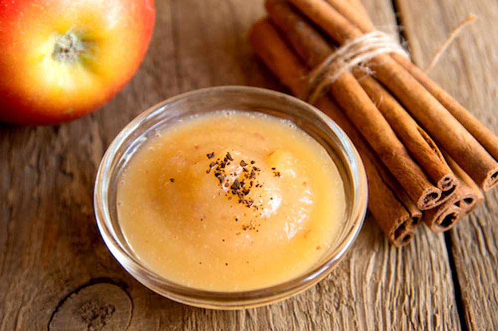 Fresh homemade applesauce (apple puree, mousse, baby food, sauce) with cinnamon (spices), spoon and apples on wooden table close up, horizontal