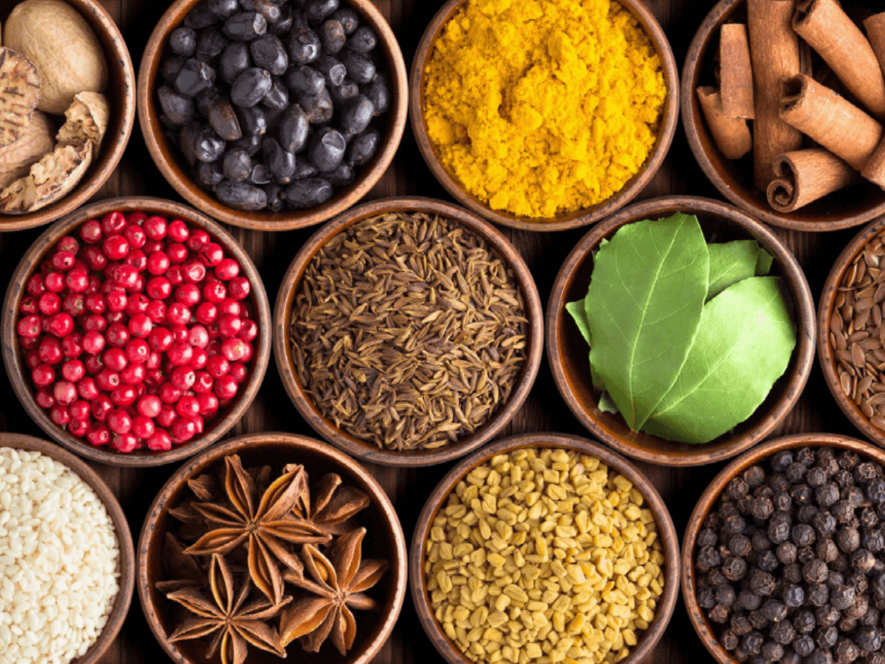 An assortment of spices and herbs arranged in wooden bowls.