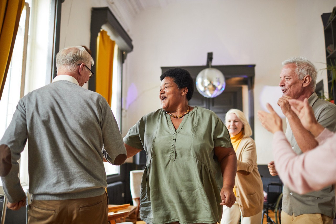 Diverse group of smiling senior people dancing while enjoying activities in retirement home, copy space