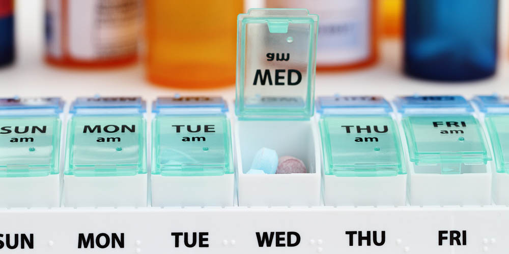 Pill organizer with daily compartments, some filled with medication.
