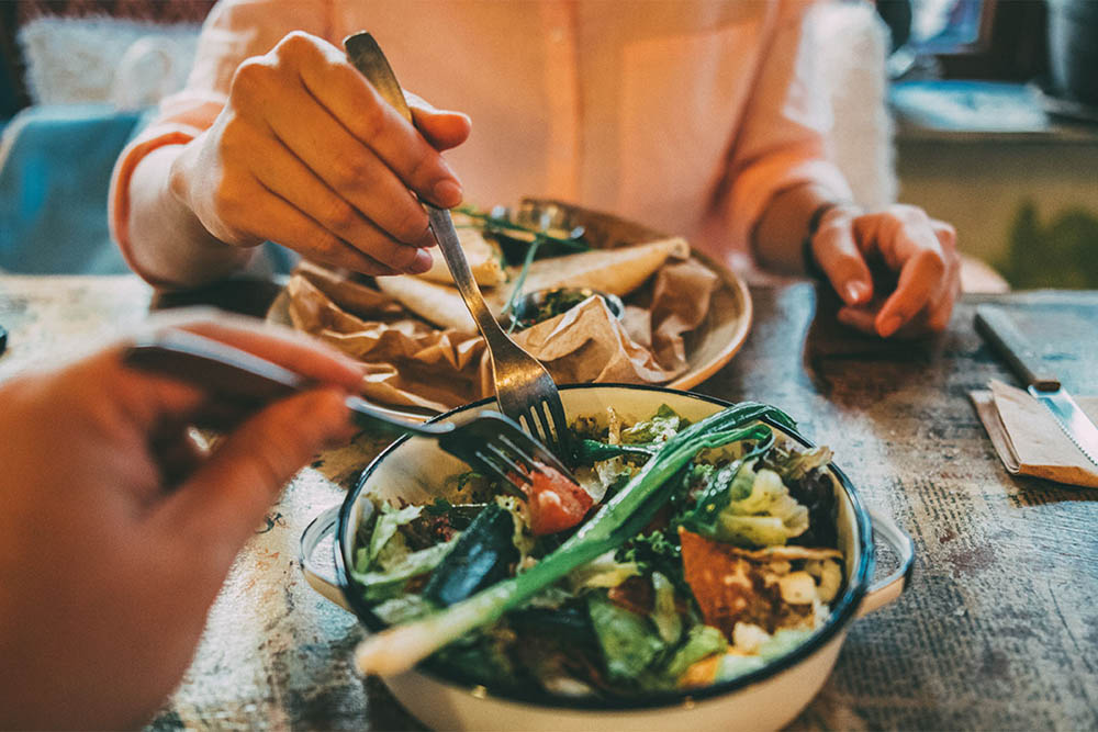 People enjoying a meal with fresh salads and tacos at a restaurant.