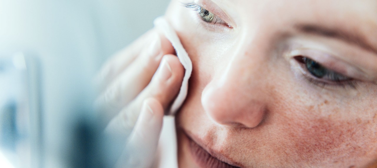 Close-up of a person gently wiping their face with a cotton pad.