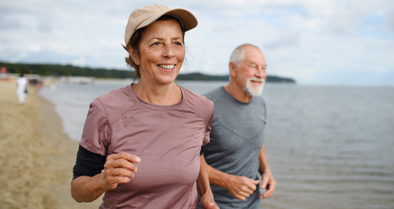 Senior couple jogging along the beach, smiling and enjoying the outdoors.