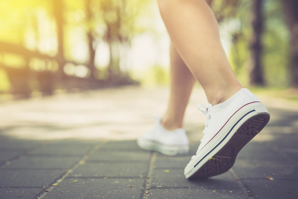 Close-up of a person walking outdoors in white sneakers.