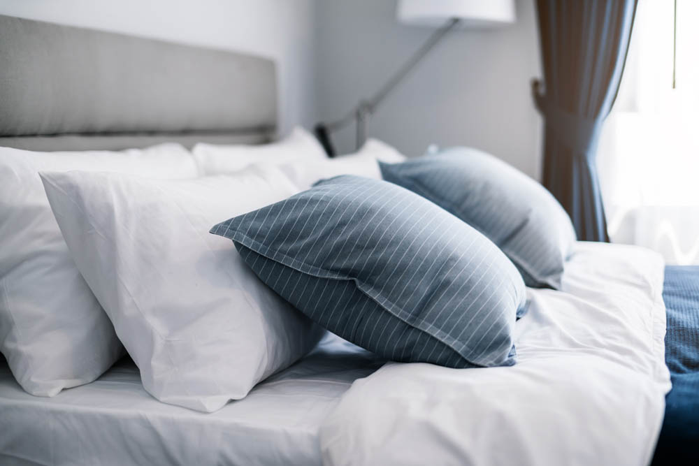Cozy bed with white linens and blue pillows near a softly lit window.