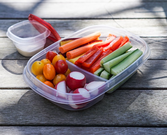 Plastic container with fresh vegetables and dip on a wooden table.