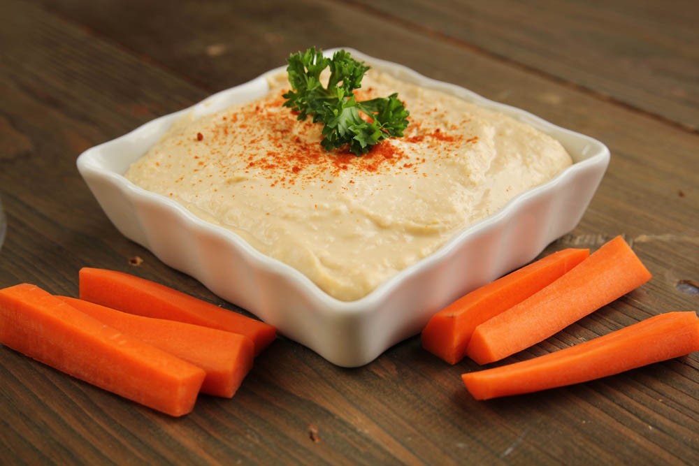 Hummus in a white container with fresh carrots