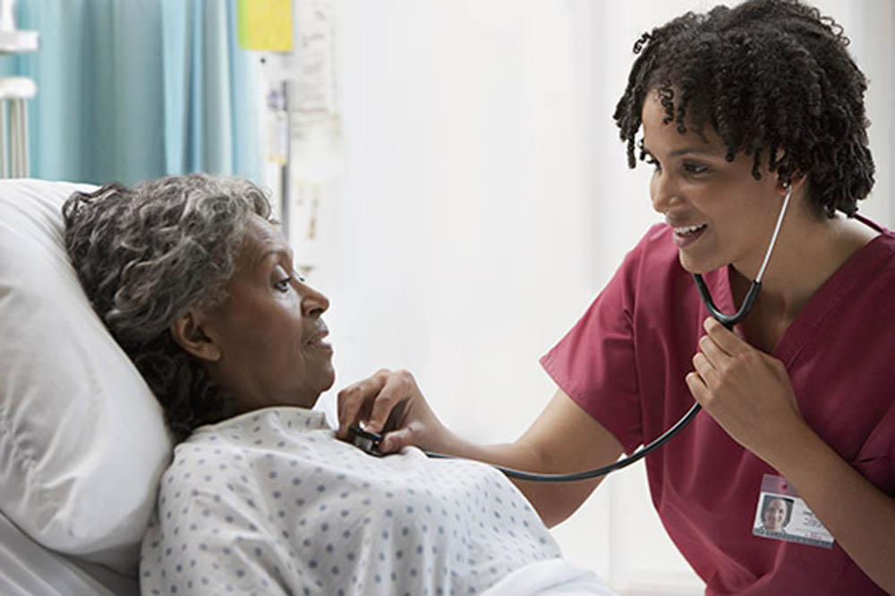 Nurse using a stethoscope to check a patient's heartbeat in a hospital bed.
