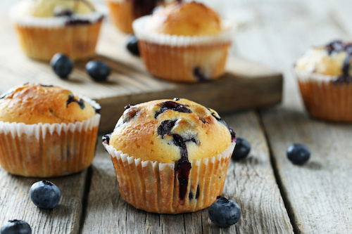 Blueberry muffins on a rustic wooden table with scattered fresh blueberries.