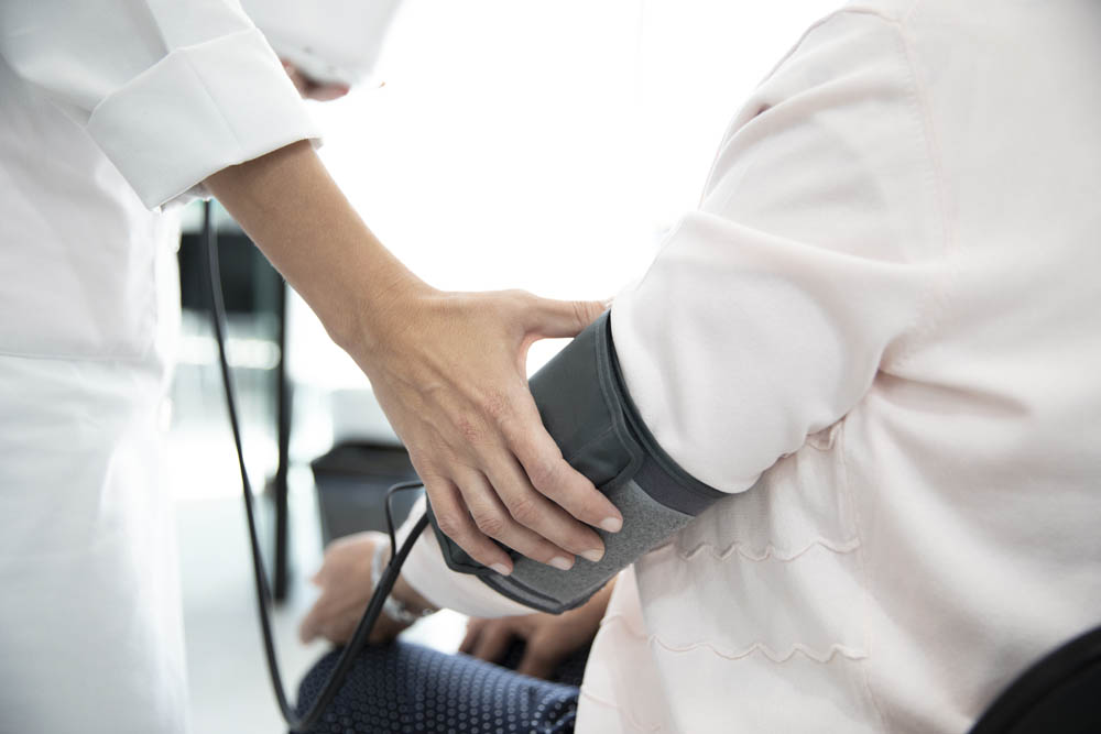 A healthcare professional measures a seated persons blood pressure using a cuff on the upper arm.