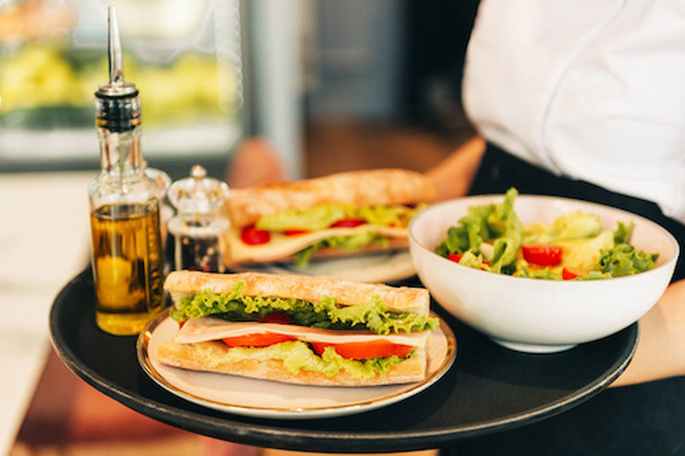 Waiter carrying tray with sandwiches and fresh green salad, cafeteria lunch