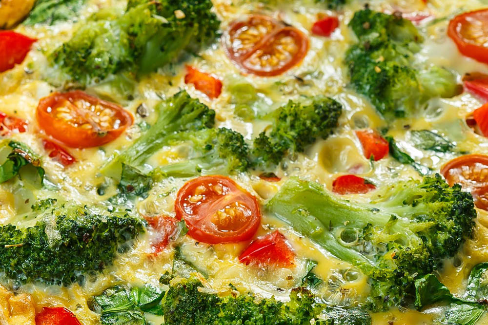 A close-up of a broccoli and cherry tomato frittata with melted cheese.