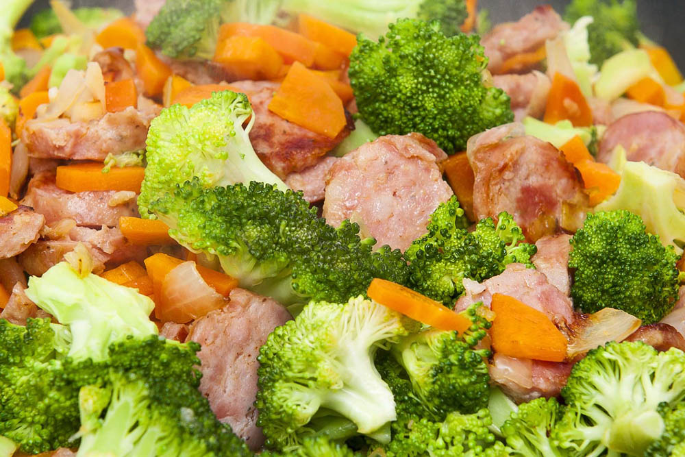 A close-up of a stir-fry with sausage, broccoli, carrots, and onions.