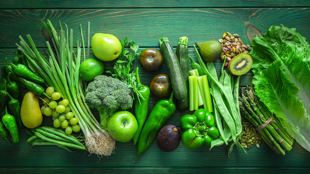 Healthy eating concepts: green table filled with a large number of green fruits and vegetables arranged in a row shot from above. The composition includes broccoli, lettuce, pear, kiwi fruit, zucchini, tomato, spinach leaves, grape, lime, green bell pepper, green beans, asparagus, avocado, parsley, pistachio and pumpkin seeds among others. High resolution 42Mp studio digital capture taken with SONY A7rII and Zeiss Batis 40mm F2.0 CF lens