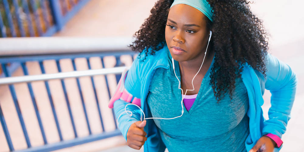 A woman is running up a set of stairs, wearing a blue athletic outfit and headphones, focused on her exercise.