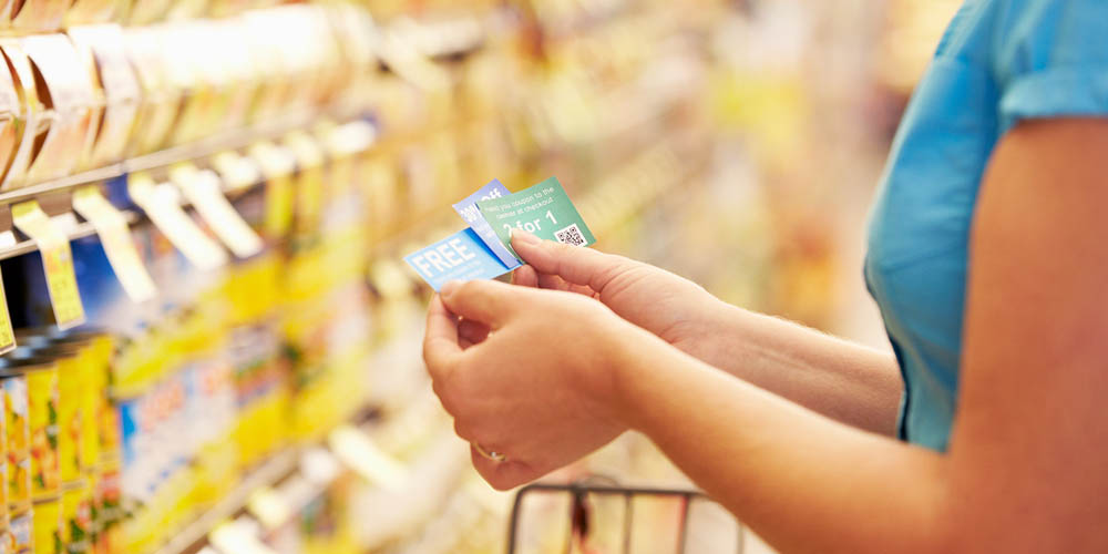 A person holding multiple store loyalty cards stands in a grocery aisle filled with products, with a blurred background of shelves.