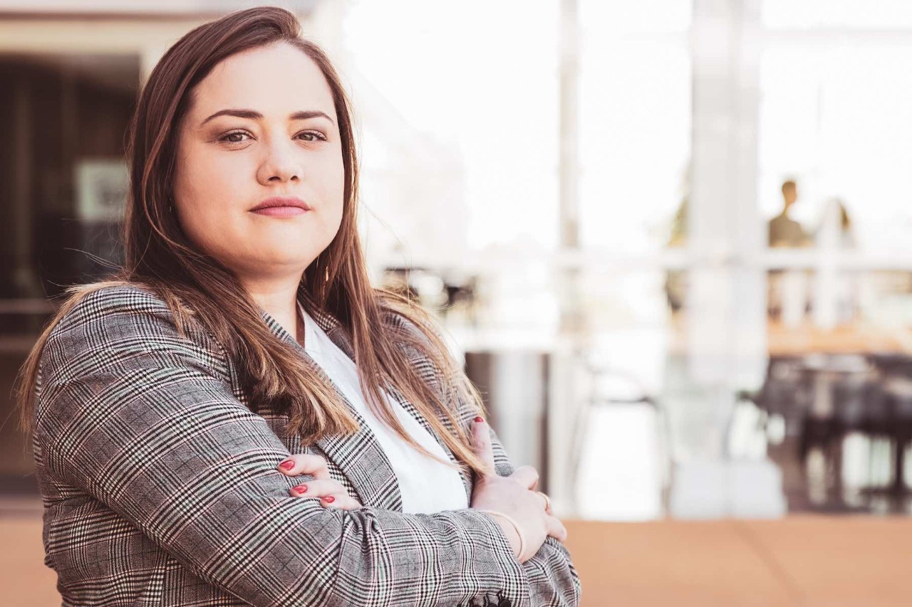 Confident business woman posing at camera outdoors. Lady looking at camera and standing with her arms crossed and blurred view in background. Business lady portrait concept.