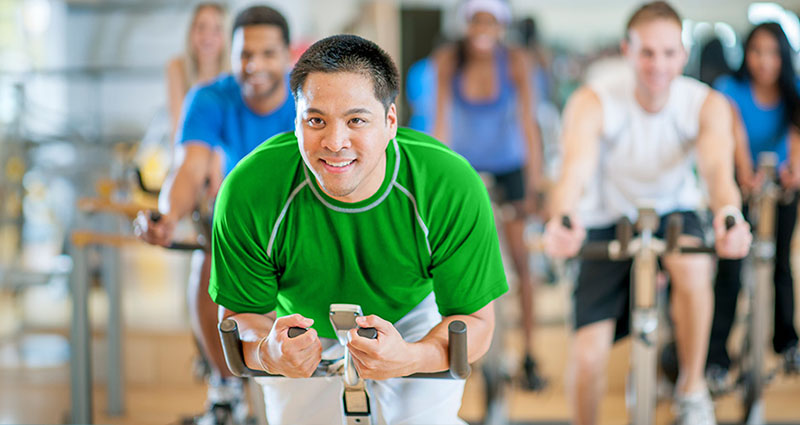 A group of people are participating in a group fitness class, with a focus on a man in a green shirt who appears to be enthusiastically engaged in the workout.
