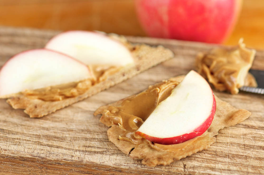 Crackers with peanut butter and apple slices on top on wooden cutting board