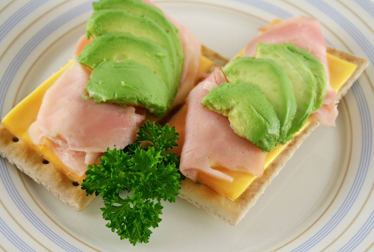 Crackers topped with cheddar cheese, turkey slices and avocado, garnished with cilantro.