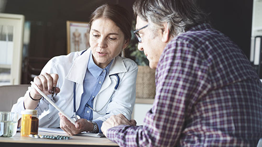A doctor explaining a prescription to a patient, with pill bottles and a glass of water on the table.