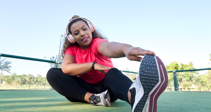Smiling woman in sportswear stretching her leg while wearing headphones outdoors.