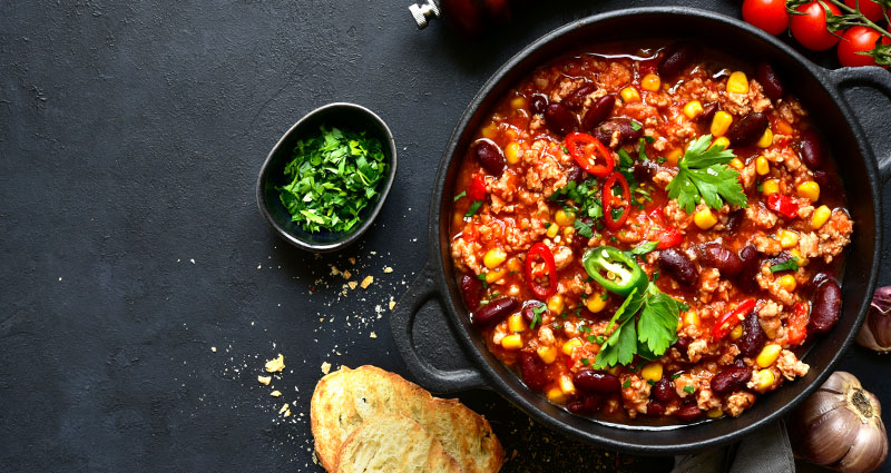 A pot filled with burrito stew served with freshly chopped cilantro and sliced peppers.