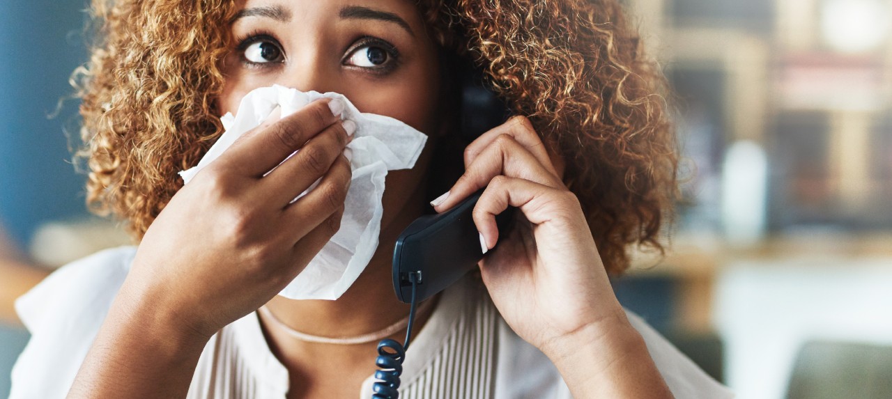 Woman holding a tissue to her nose while talking on the phone, appearing to have a sinus infection