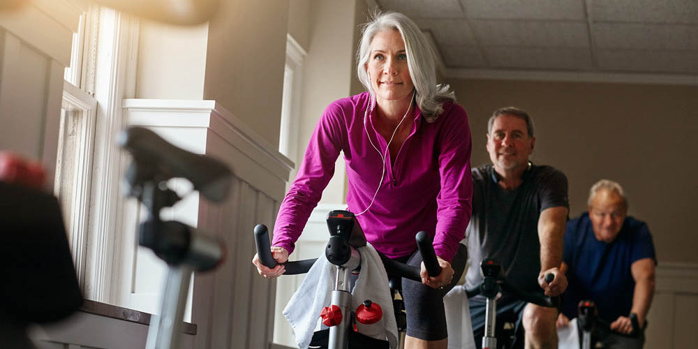 Older woman in a purple jacket leading a group cycling class at the gym, smiling with enthusiasm
