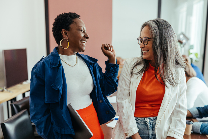 Two women smiling and talking in an office setting.