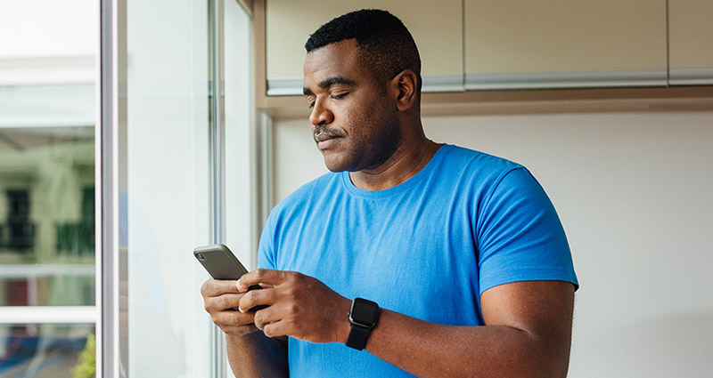 Man in a blue shirt using his smartphone near a window