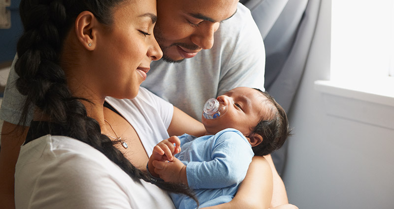 Smiling parents holding their newborn baby with a pacifier.