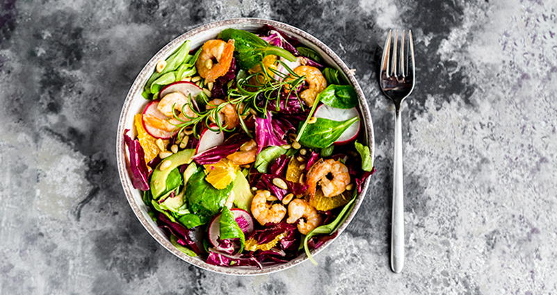 A salad bowl filled with healthy greens, avocado, shrimp and sliced oranges.