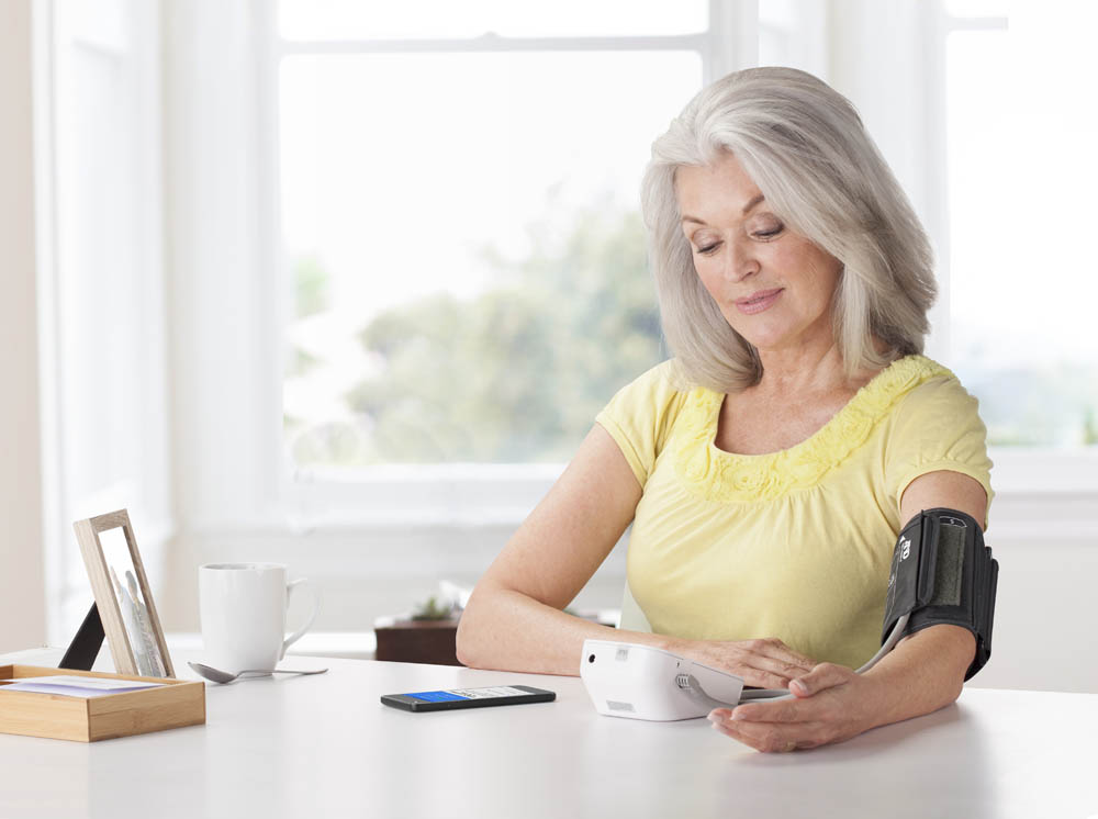 Elderly woman in a yellow shirt checking her blood pressure at home.