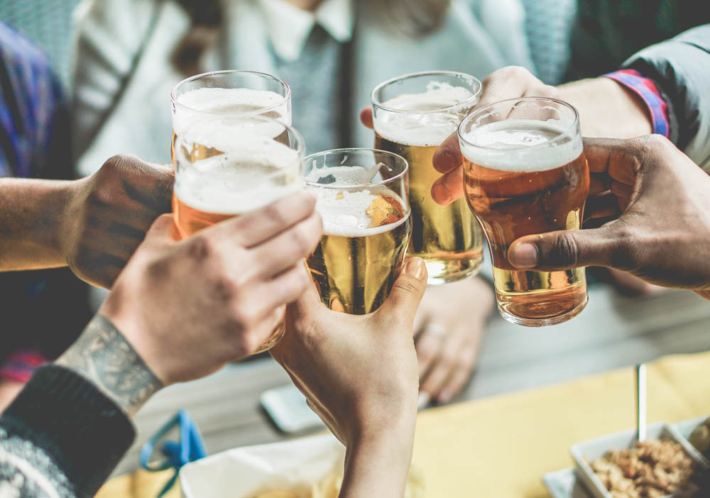 Multiracial group of friends enjoying a beer - Young people hands toasting and cheering aperitif beers half pint - Friendship and youth concept - Warm vintage filter - Focus on bottom hand