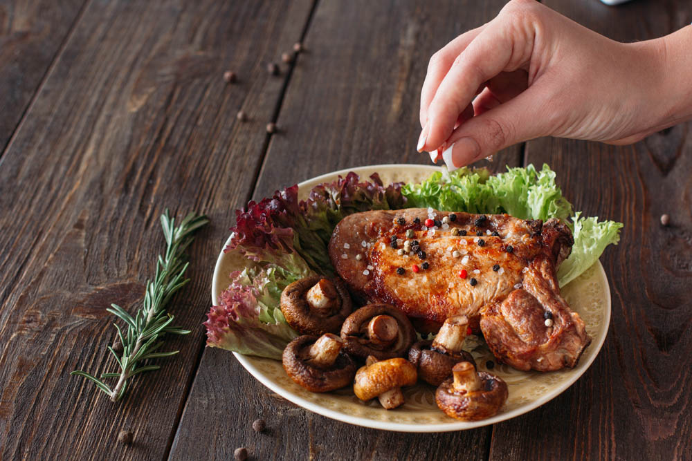 Cooking pork dish with lettuce and mushrooms. Chief adding herbs and spicy to grilled steak. Decorating food for retail.