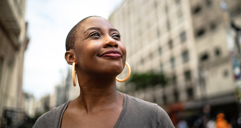 Confident woman with short hair and gold hoop earrings looking up while standing in a bustling city street