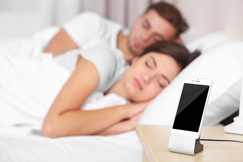 Happy couple waking up with mobile alarm clock