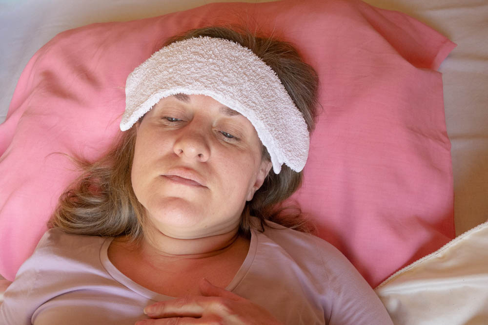 Middle aged woman has a fever or abnormal blood pressure. 40 years women lying in the bed with wet compress on a head. She is unwell and sick. Girl close-up portrait with health problems