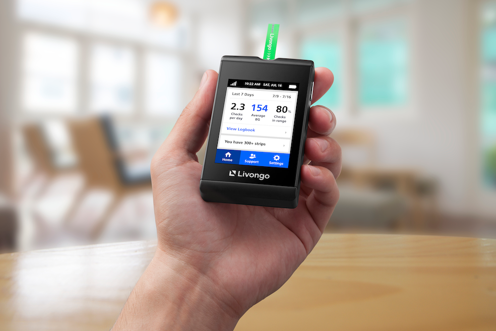 A hand holds a Livongo blood glucose meter displaying recent readings.