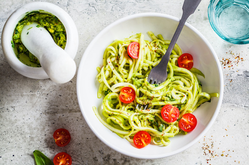 Zucchini pasta with pesto, avocado and tomatoes in a white plate. Raw vegan food concept.