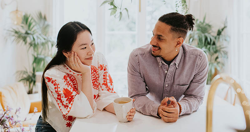  A man and woman are sitting at a table, smiling and engaging in a conversation, with a warm and friendly atmosphere.