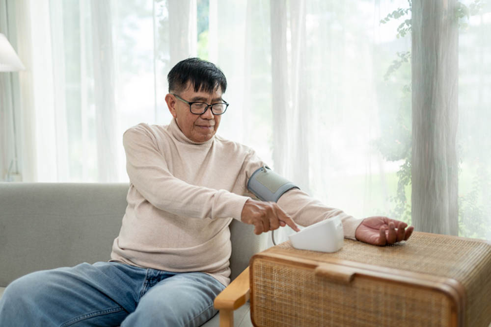 Man sitting on a couch checking his blood pressure with a monitor.