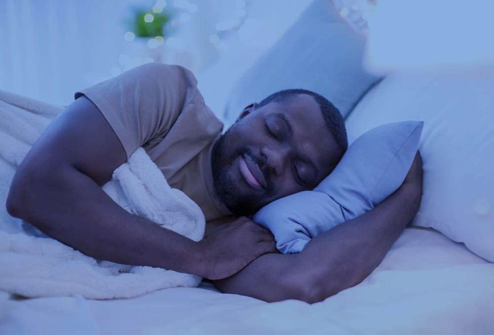 Man sleeping peacefully on his side in bed, with a light blue pillow and cozy white blanket.