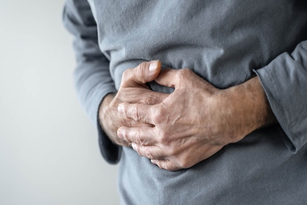 Man clutching his stomach in discomfort, wearing a gray sweater.