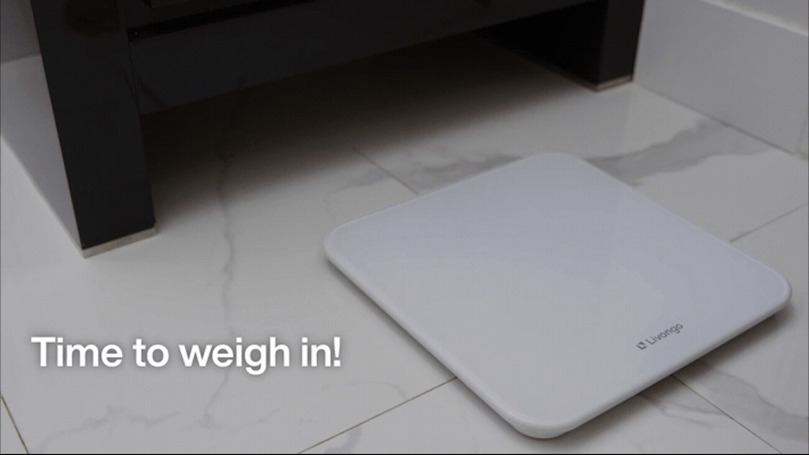 Digital bathroom scale on a tiled floor, with the text Time to weigh in! visible above it.