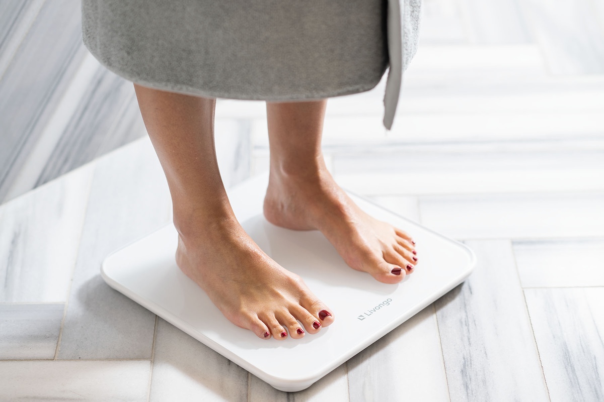 Person standing on a white digital scale, wearing a gray robe, on a patterned tile floor.