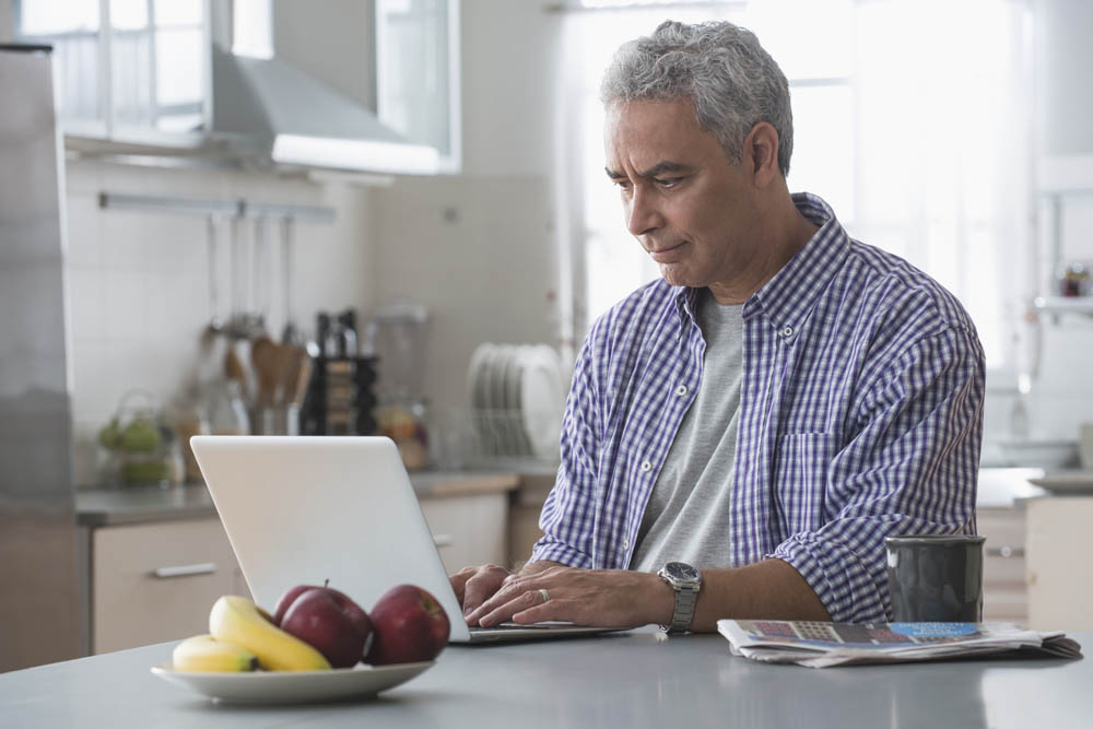 Hispanic man using laptop at kitchen table